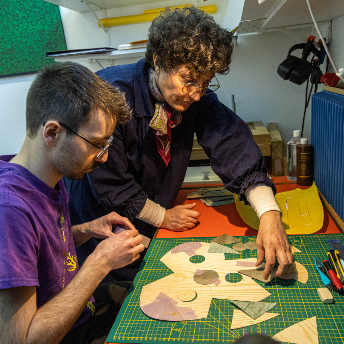 Participant guidé par l'artisane d'art pour assembler des motifs en placages de bois sur un tabouret lors de l’atelier marqueterie bois. Un moment d’échange et de création artisanale.