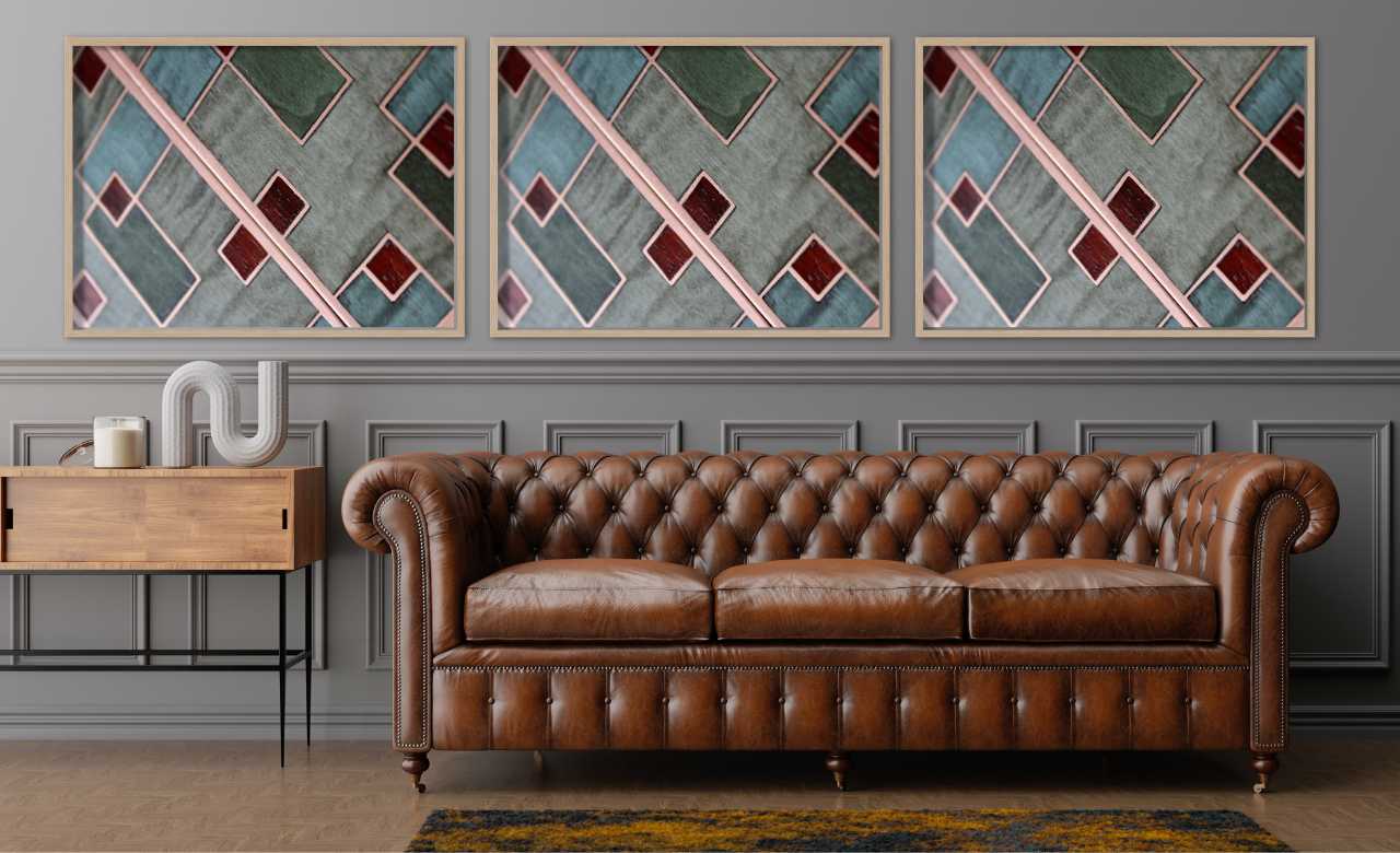 Triptyque mural en marqueterie cloisonnée d'Atelier Nathalie Melon, composé de motifs géométriques en bois et cuivre, présenté dans un salon luxueux avec un canapé Chesterfield en cuir et une console en bois.