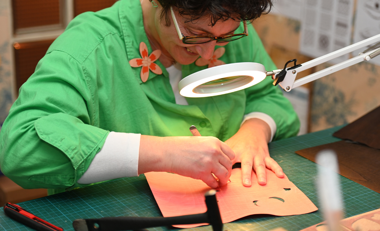 Artisane d’art réalisant une découpe minutieuse sur un placage de bois teinté, illustrant la précision et le savoir-faire manuel de la marqueterie cloisonnée. Atelier Nathalie Melon