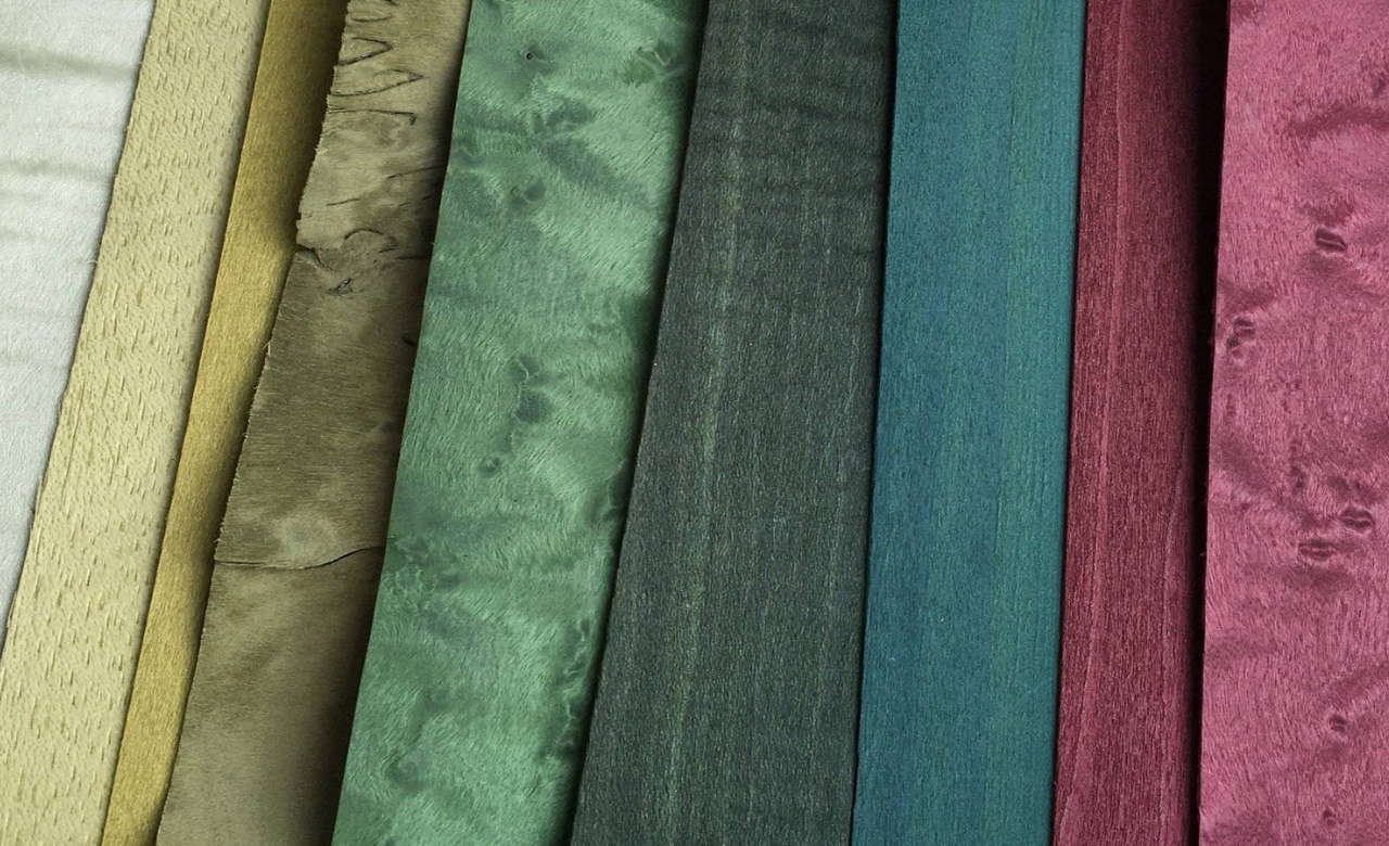 Sélection de placages de bois teintés aux textures variées, allant du beige au vert profond et au bordeaux. Illustration des matières nobles et raffinées utilisées par l'Atelier Nathalie Melon pour des créations en marqueterie cloisonnée alliant esthétisme et savoir-faire artisanal.